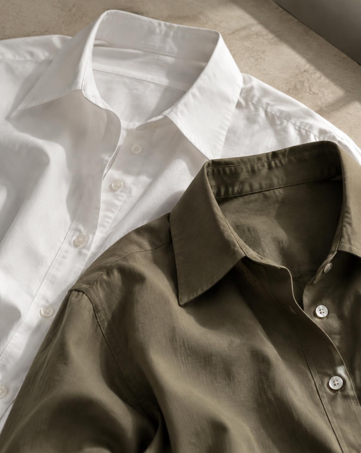 A crisp white shirt and an olive shirt laid flat, collars open, in soft daylight